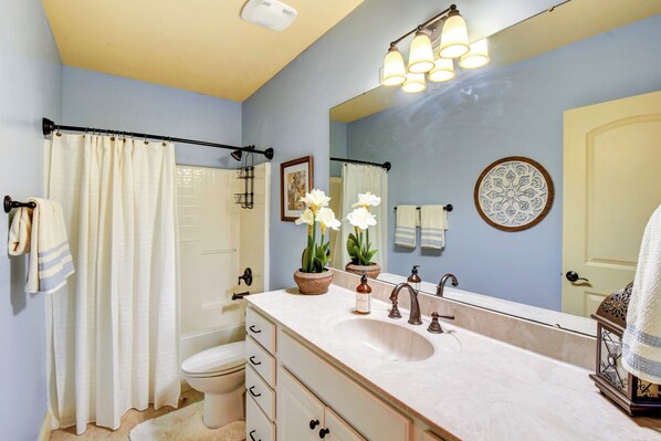 Une salle de bain avec un lavabo, un miroir et des toilettes. Des serviettes sont accrochées au mur et il y a un rideau de douche.