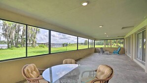 Un patio techado con una mesa de vidrio y sillas de mimbre, con vistas a un paisaje verde y un cuerpo de agua.