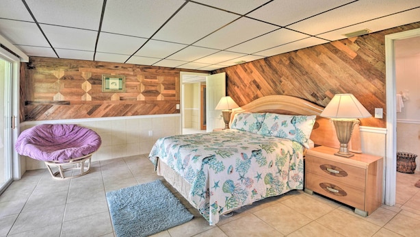 Un dormitorio con cama, mesitas de noche, una silla y una pared de madera decorativa.