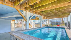 An indoor swimming pool with a tiled edge, supported by a wooden ceiling structure, and surrounded by a fenced area with a view of residential buildings. - Waterfront Home w/ Deck in North Myrtle Beach! (North Myrtle Beach)