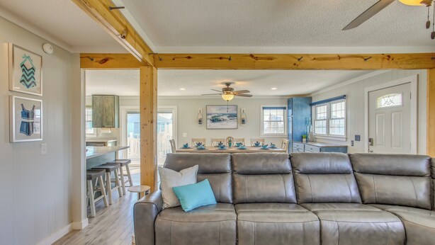 A spacious living room with a leather sofa, wooden ceiling beams, and a dining area in the background. - Waterfront Home w/ Deck in North Myrtle Beach! (North Myrtle Beach)