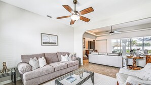 A spacious living room with a grey sofa, a coffee table, and a ceiling fan. - Marco Island Home w/ Screened Pool < 1 Mi to Beach (Marco Island)
