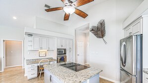 A kitchen with white cabinets, a stainless steel refrigerator, a built-in oven, and a ceiling fan. - Marco Island Home w/ Screened Pool < 1 Mi to Beach (Marco Island)