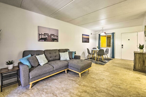 A living room with a sectional sofa, a dining area with a table and chairs, and a kitchen area with a cabinet.