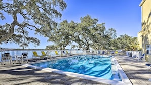 Ein rechteckiger Swimmingpool mit einer gefliesten Liegefläche, umgeben von Liegestühlen und Bäumen.