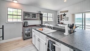 A modern kitchen with white cabinetry, a granite countertop, and a large window providing a view of the outdoors.