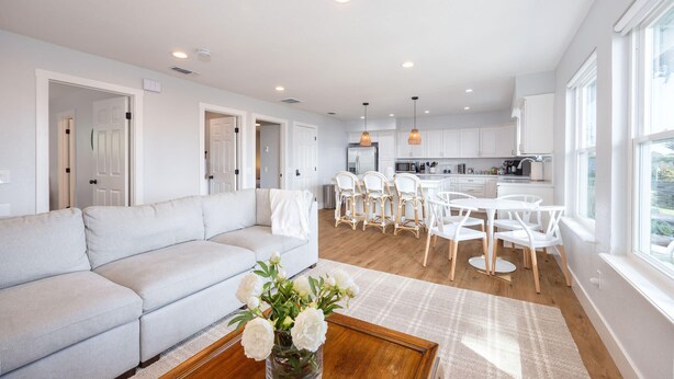A modern living room with a sofa, a dining table with chairs, and a kitchen in the background.