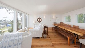 A spacious room with a large wooden dining table, white walls, and a view of the outdoors.