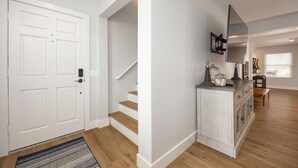 A hallway with a white door, wooden stairs, a white cabinet, and a bench.