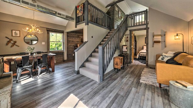 A spacious living area with a staircase, wooden flooring, a dining table with chairs, a sofa, and a chandelier. - The Reubling House - Modern-rustic Cabin! (Defiance)