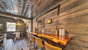 A rustic kitchen with a wooden bar, bar stools, and a chandelier. - The Reubling House - Modern-rustic Cabin! (Defiance)
