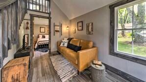 A cozy living room with a leather sofa, a staircase, and a large window offering a view of the outdoors. - The Reubling House - Modern-rustic Cabin! (Defiance)