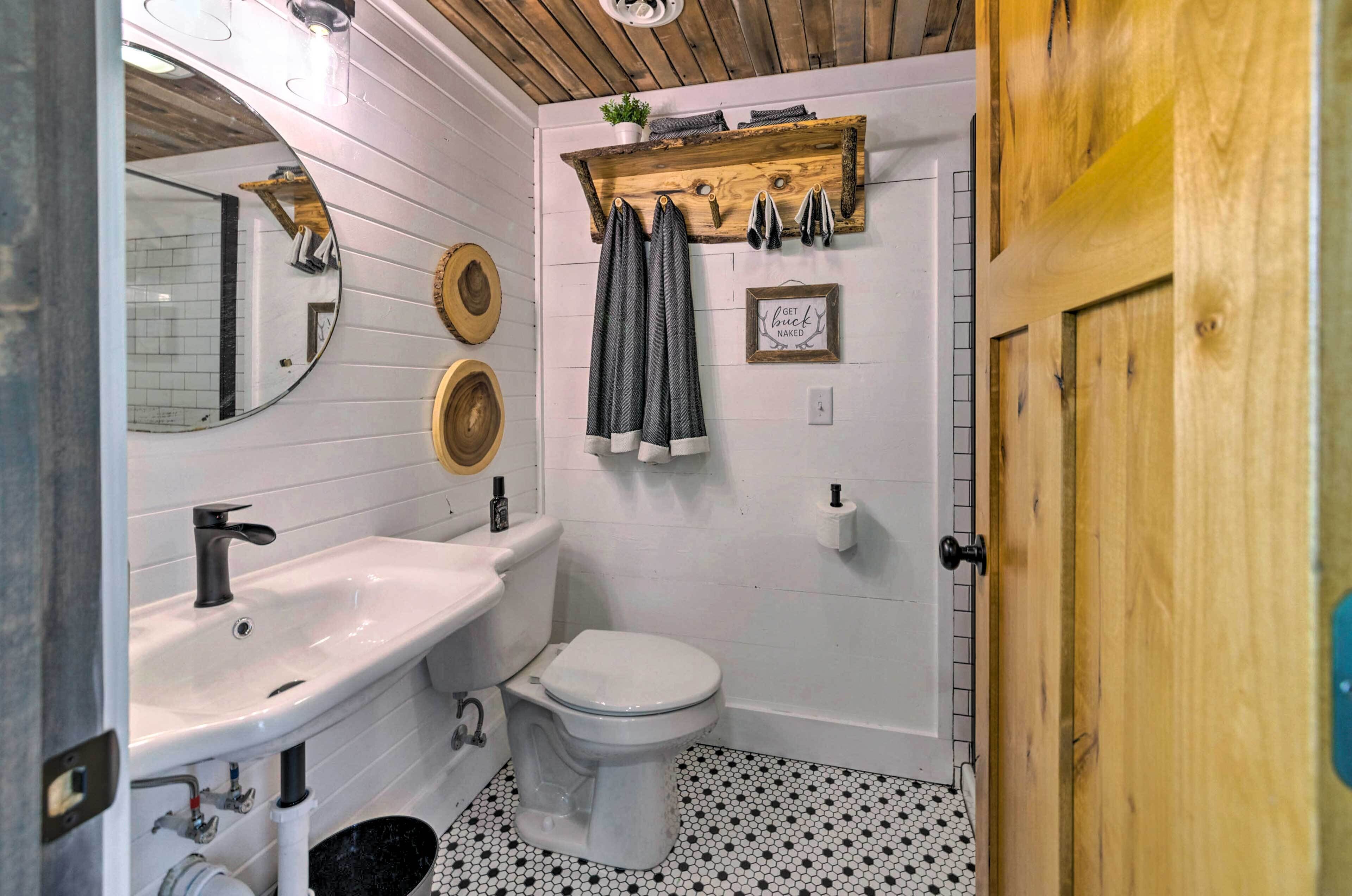 A bathroom with a white sink, toilet, and wooden vanity. There is a mirror, a towel rack, and a small plant on the vanity.
