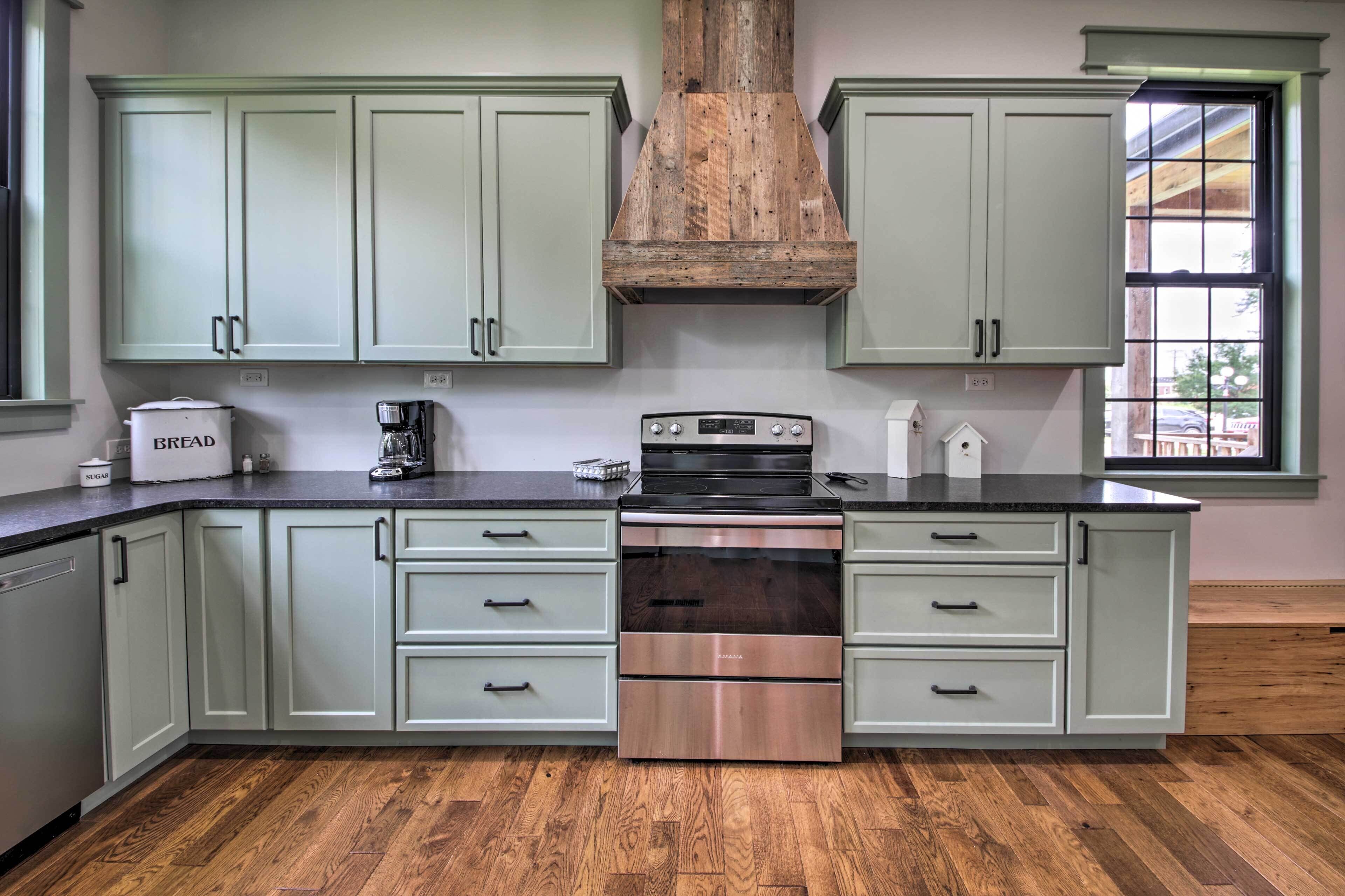 A kitchen with light green cabinets, a stainless steel stove, and a window with a view of the outside.