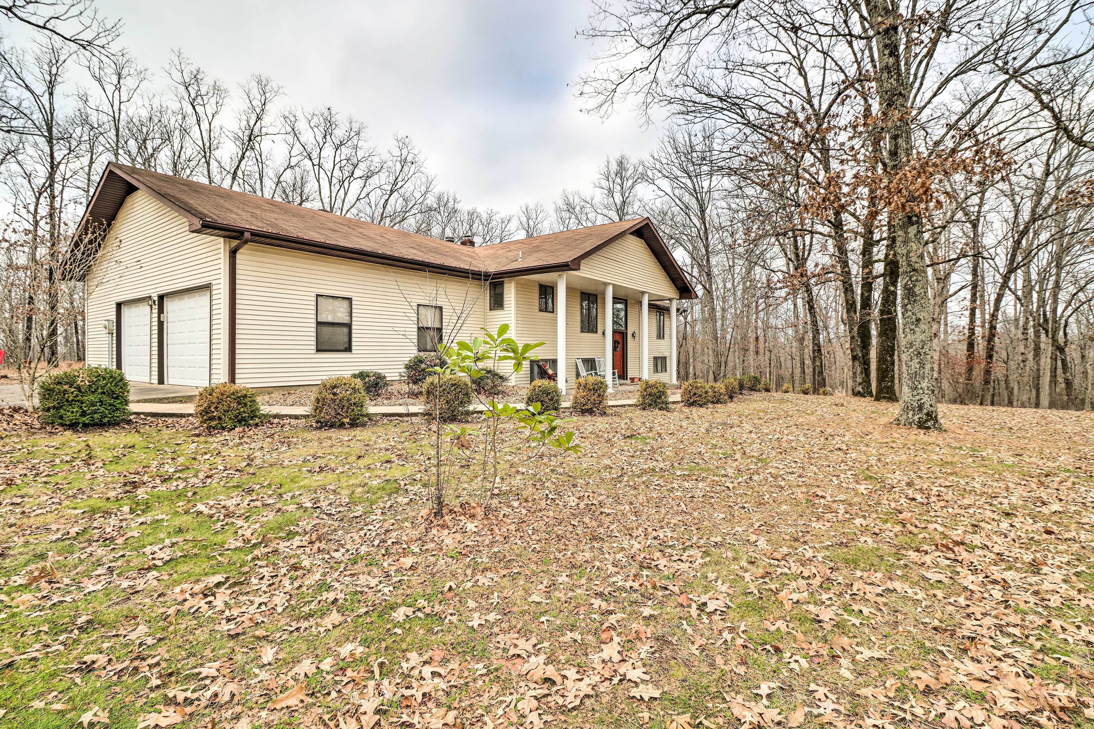 A two-story house with a front porch, surrounded by a wooded area.