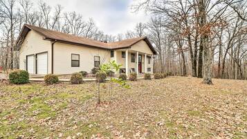 A two-story house with a front porch, surrounded by a wooded area.