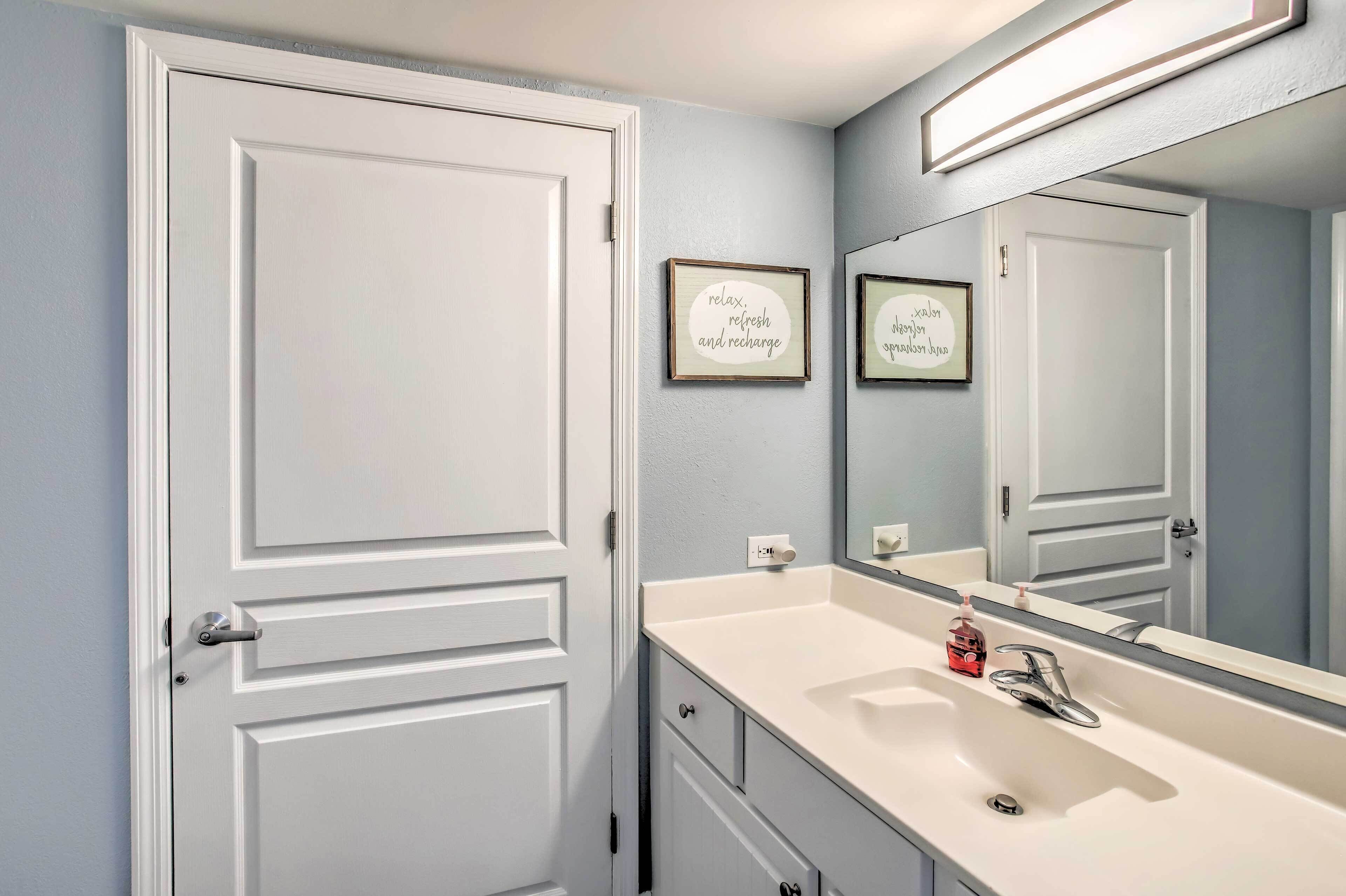 A bathroom with a white vanity, a mirror, and two framed signs on the wall.