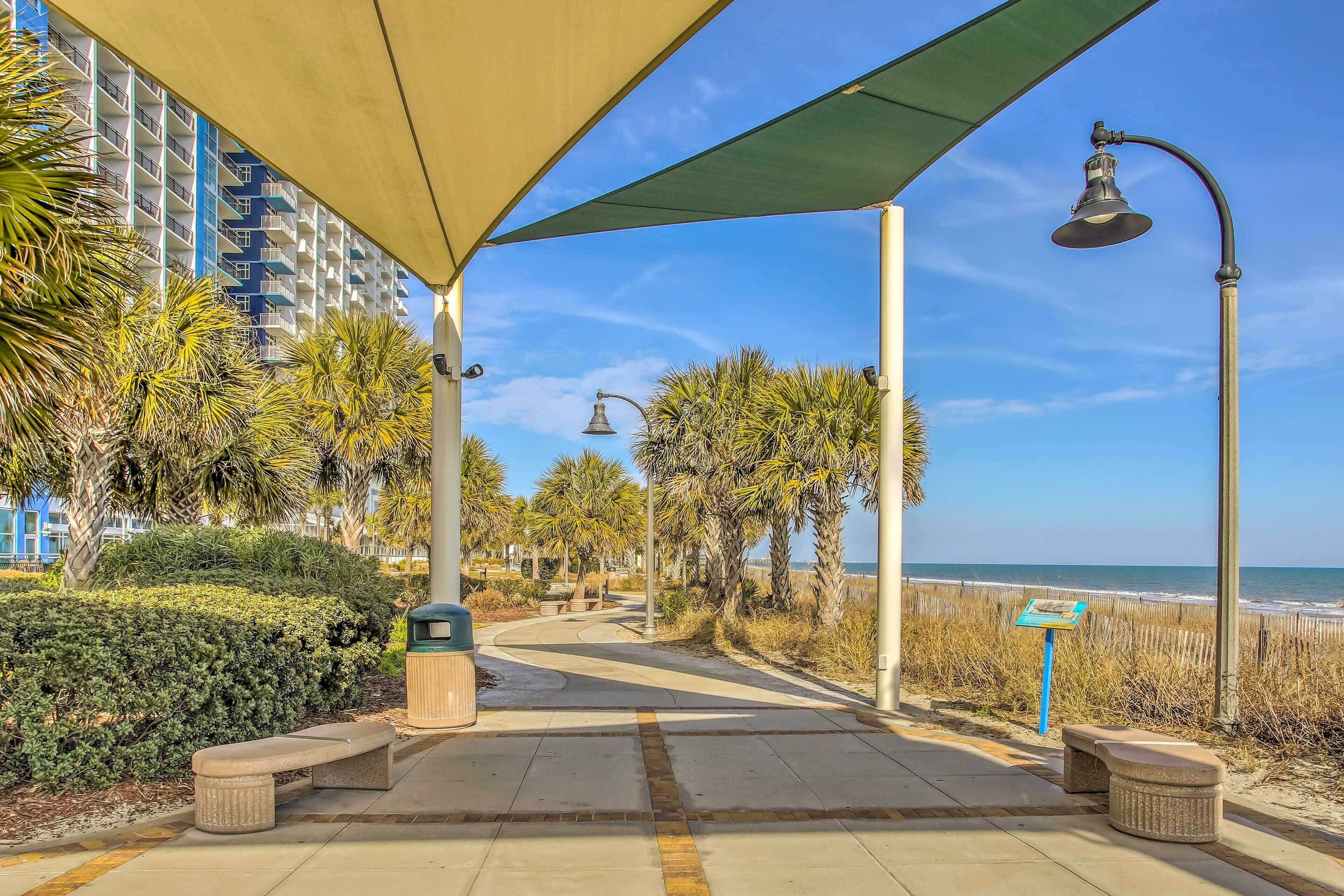 A pathway with benches, a trash bin, and a beach view.