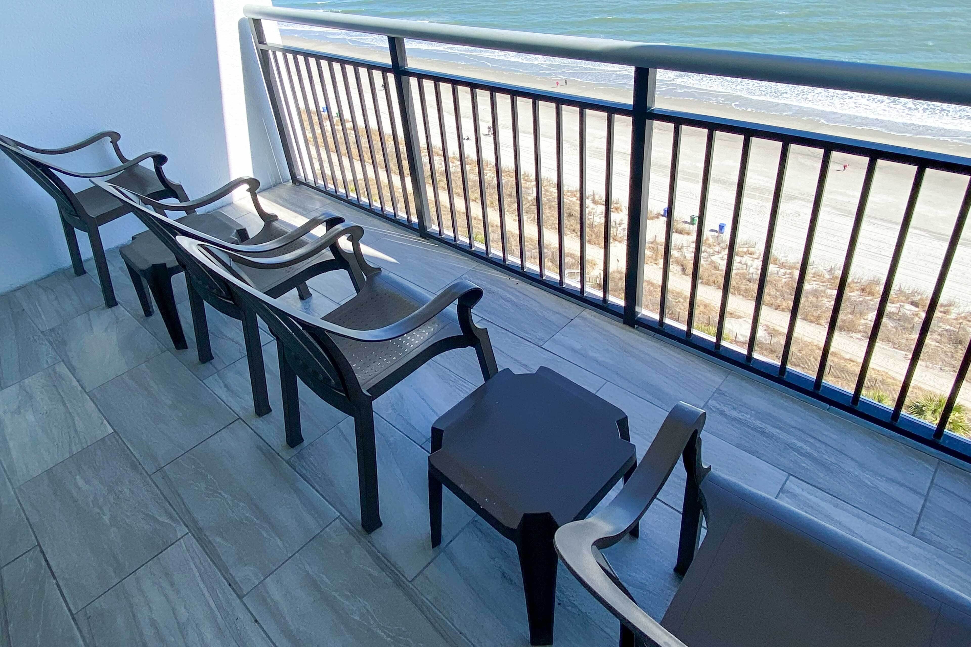 Een balkon met uitzicht op het strand, met een tafel en vier stoelen.