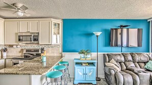 A kitchen with a microwave, stove, and bar stools. There is a blue cabinet with a plant and a leather couch. - Beachfront Murrells Inlet Condo w/ Ocean Views (Murrells Inlet)