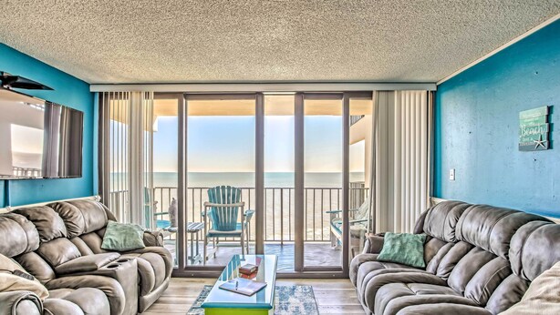 A living room with a large window overlooking a balcony with a view of the ocean. - Beachfront Murrells Inlet Condo w/ Ocean Views (Murrells Inlet)