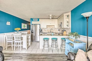 A kitchen with white cabinets, a refrigerator, and a blue accent wall. - Beachfront Murrells Inlet Condo w/ Ocean Views (Murrells Inlet)