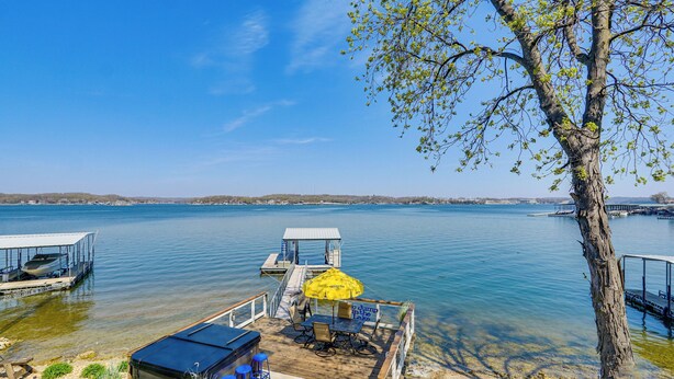 Un pontile sul lago con un tavolo e sedie, un ombrellone giallo e un molo con una barca.