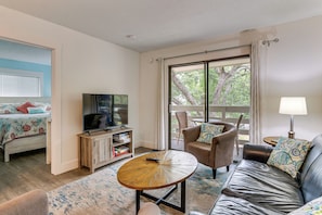 Une chambre avec un lit, une télévision, un canapé, une chaise, une table et un balcon avec vue.