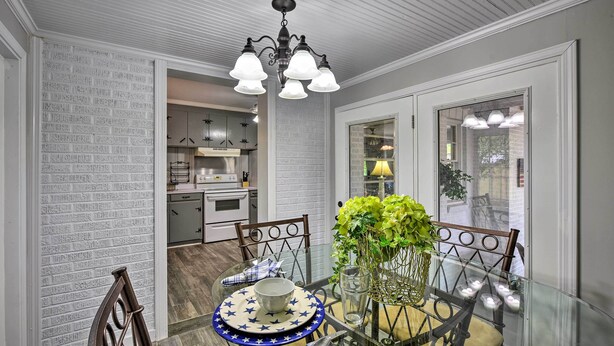 A dining area with a glass table, chairs, a chandelier, and a view of the kitchen.