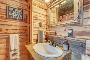Un baño de estilo cabaña con interior de madera, un lavamanos, un espejo y un perchero para toallas.
