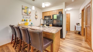 A kitchen with a central island, bar stools, wooden cabinets, a refrigerator, and a microwave. - Accessible Branson Condo: Balcony + Lake Access! (Branson West)