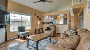 A spacious living room with a large window, a ceiling fan, a kitchen in the background, and a brown leather couch. - Branson Condo w/ Pool: 2 Mi to Table Rock Lake (Branson)
