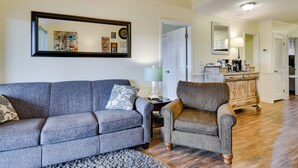 A living room with a gray sofa, a brown armchair, and a coffee table. There is a painting on the wall and a mirror above the sofa. - Branson Condo w/ Views - Near Silver Dollar City! (Branson West)