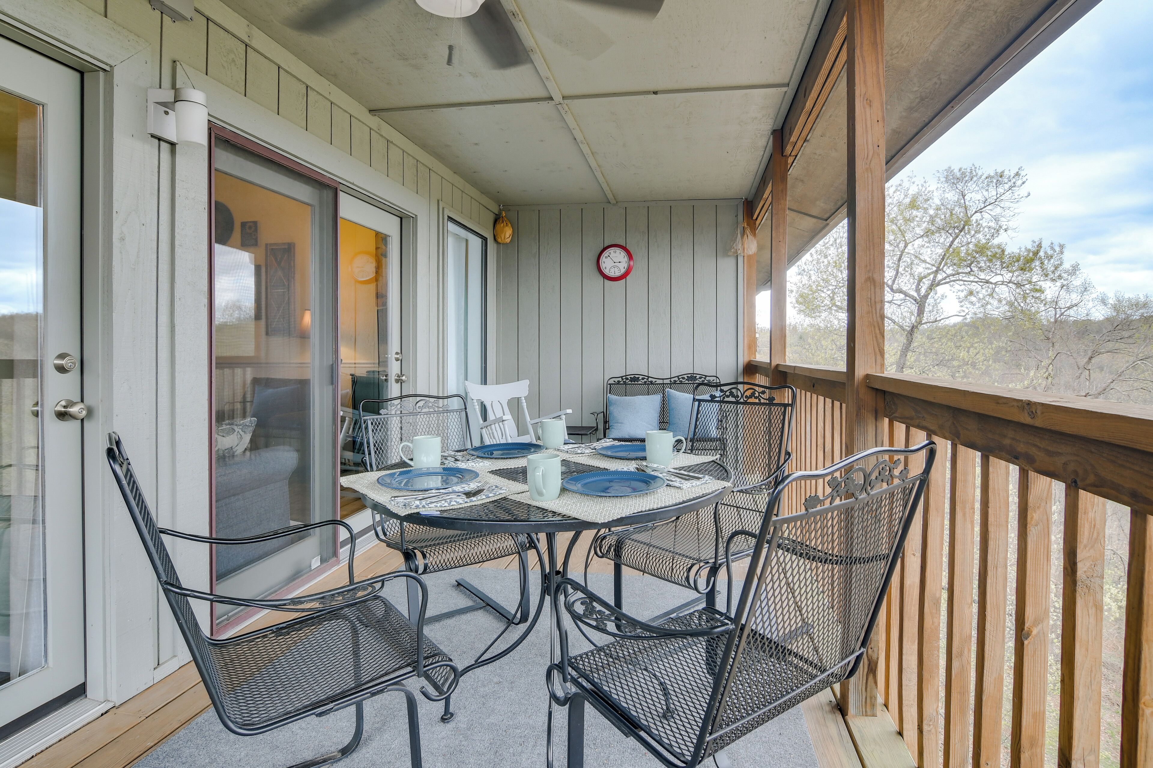 Un patio cubierto con una mesa lista para cuatro personas, sillas de metal y vistas del paisaje circundante.