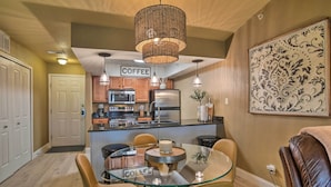 Una cuina moderna amb una taula de dinar de vidre, una zona de cafè i una gran obra decorativa a la paret.