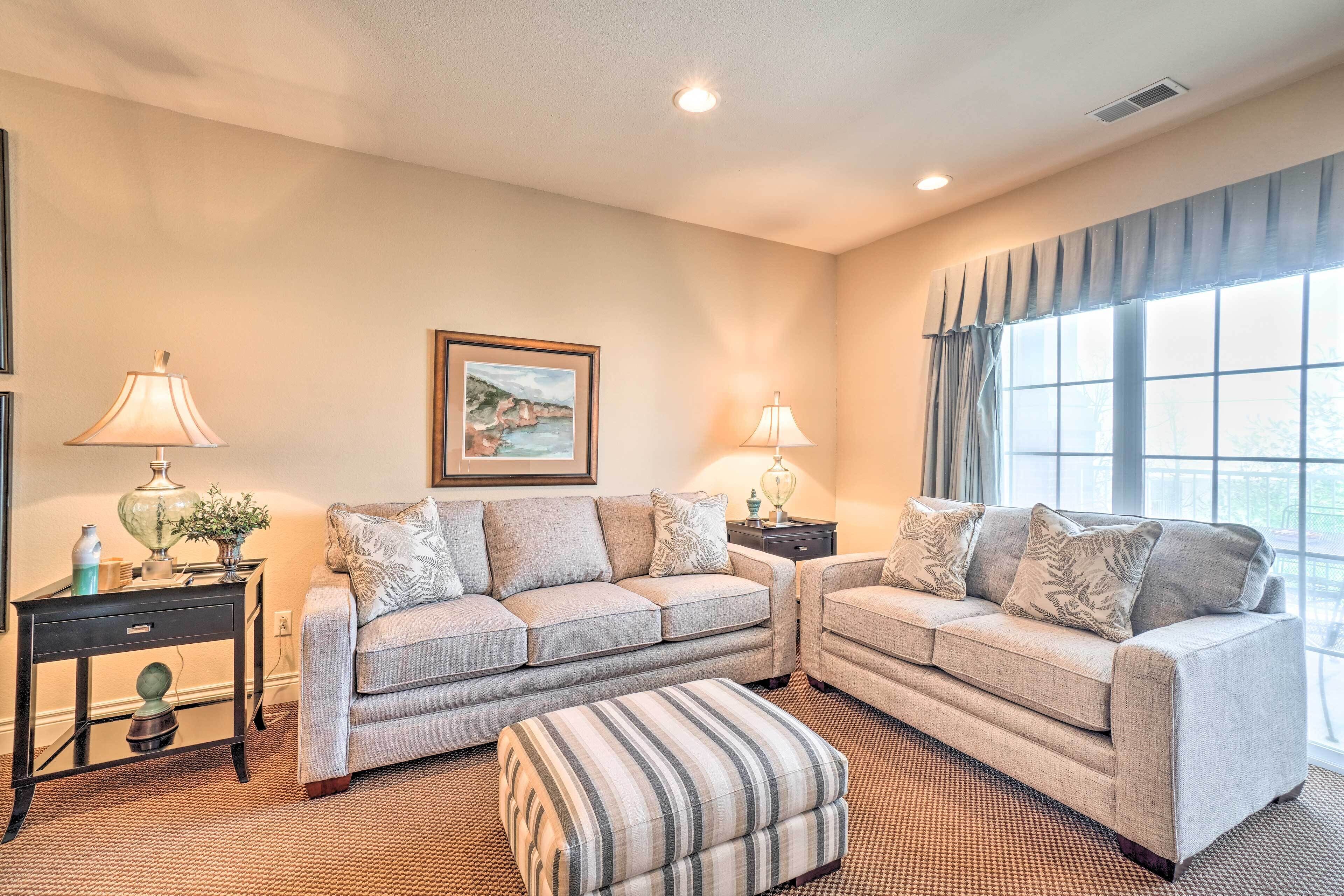 A living room with two sofas, a striped ottoman, and a framed picture on the wall.