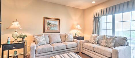 A living room with two sofas, a striped ottoman, and a framed picture on the wall.