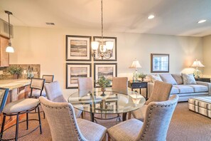 A modern living room with a glass dining table surrounded by cushioned chairs, a sofa, and a coffee table.