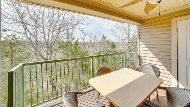 A covered outdoor area with a table and chairs, a green railing, and a view of trees and hills. - Branson Condo w/ Balcony, Near Silver Dollar City! (Branson)