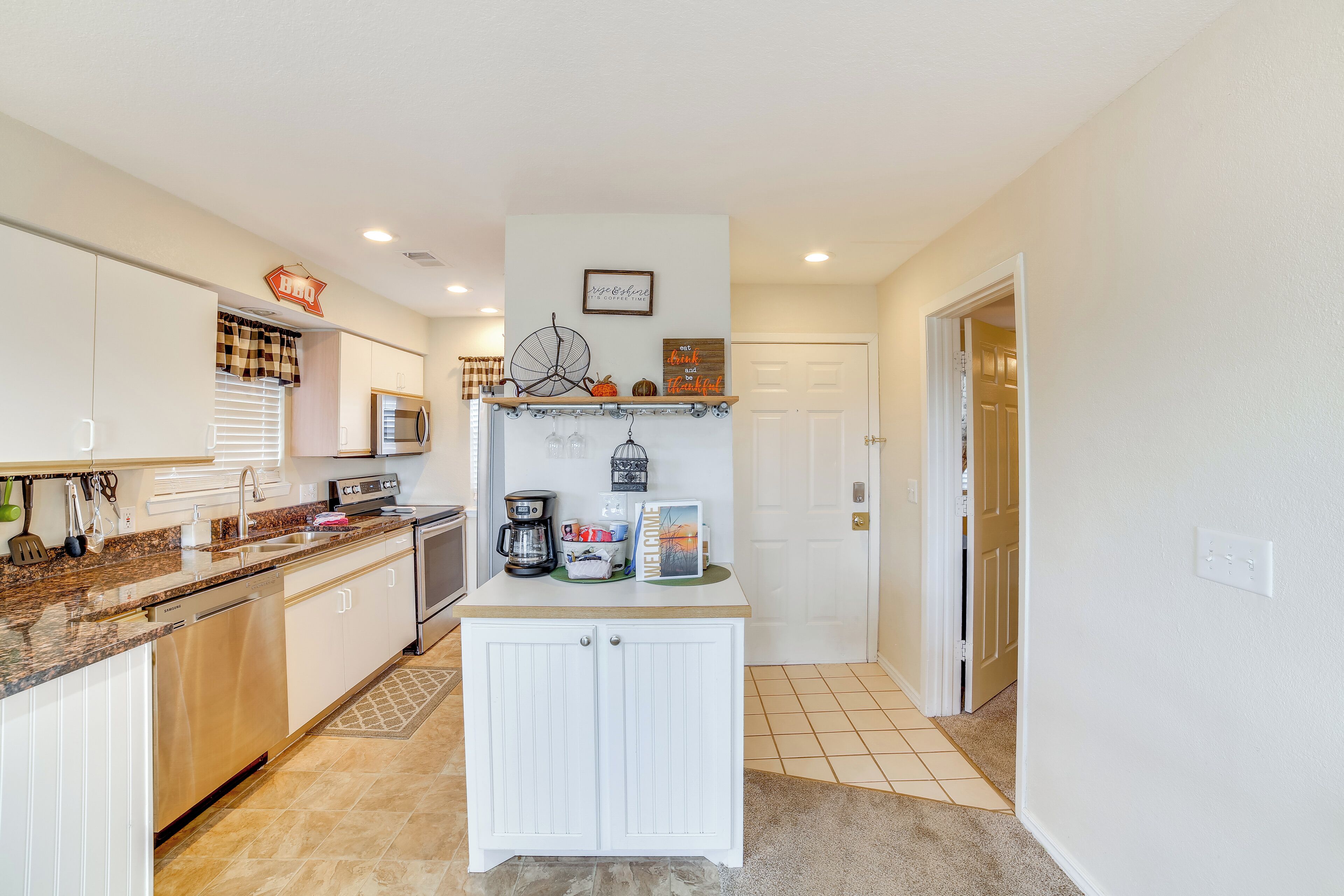 A modern kitchen with white cabinetry, a granite countertop, and a built-in microwave. There is a coffee maker, a toaster, and a small shelf with decorative items.