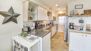 A modern kitchen with white cabinetry, granite countertops, and stainless steel appliances. There is a decorative star on the wall and a welcome sign above the sink. - Branson Condo w/ Balcony, Near Silver Dollar City! (Branson)
