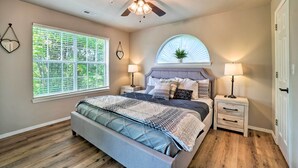 A bedroom with a bed, two bedside tables, a ceiling fan, a window with blinds, and a wall-mounted plant. - Branson Condo ~ 6 Mi to Silver Dollar City! (Branson)