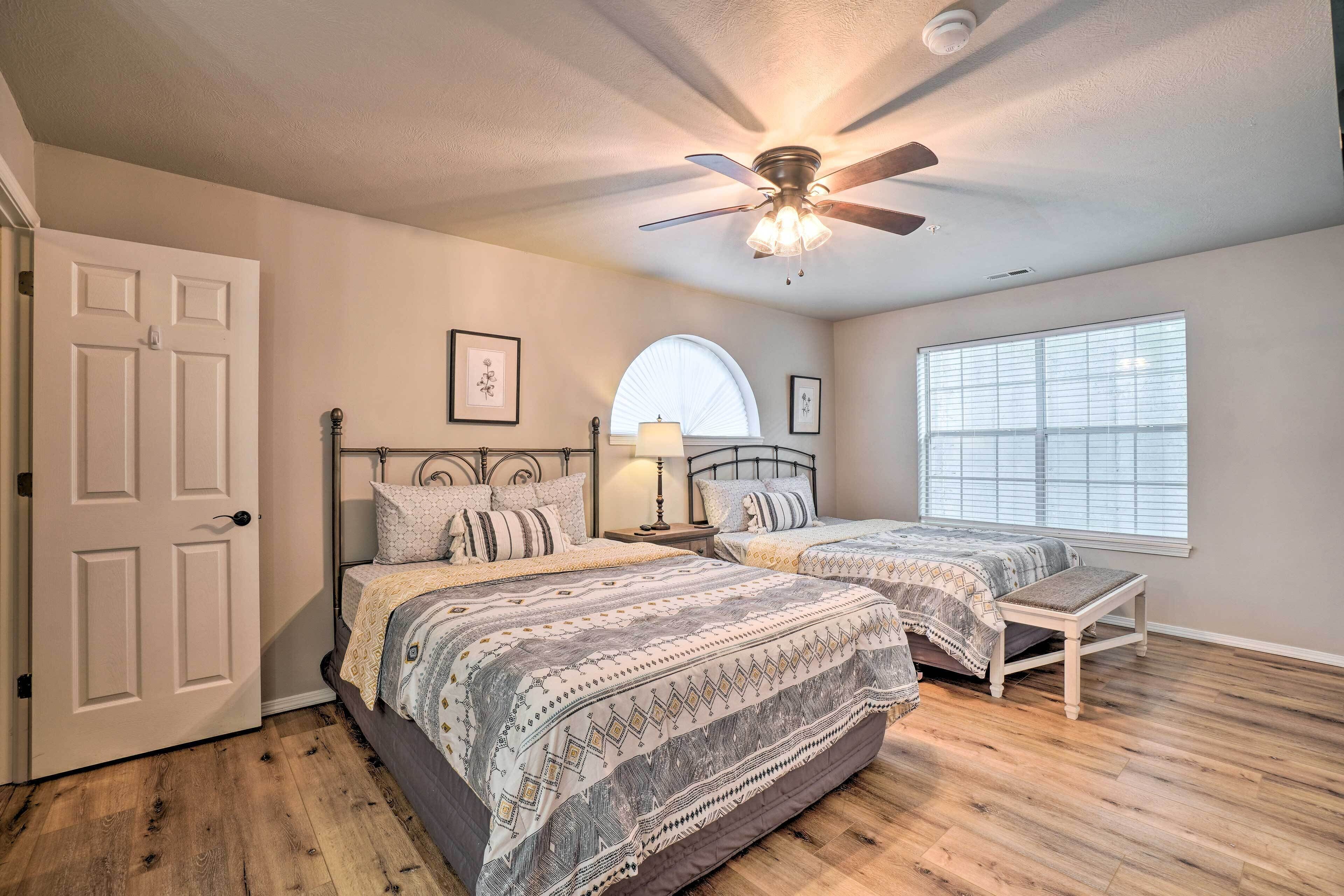 A bedroom with two beds, a ceiling fan, a large window, and hardwood flooring.