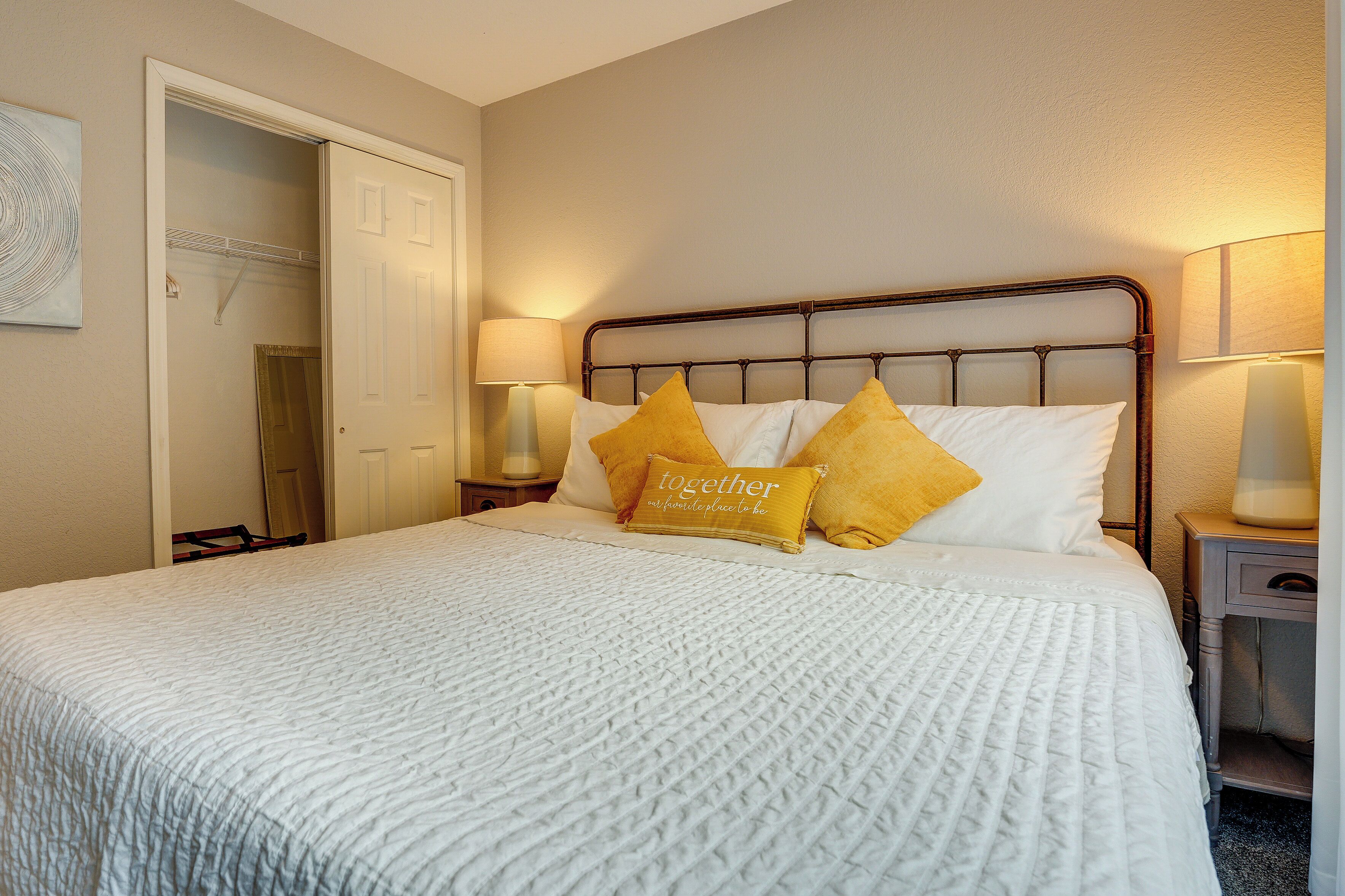 A neatly made bed with a white comforter and two yellow pillows, a bedside lamp, and a door leading to a closet.