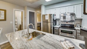 A modern kitchen with stainless steel appliances, a marble countertop, and white cabinetry. - Family-friendly Condo: 1 Mi to Silver Dollar City! (Branson West)