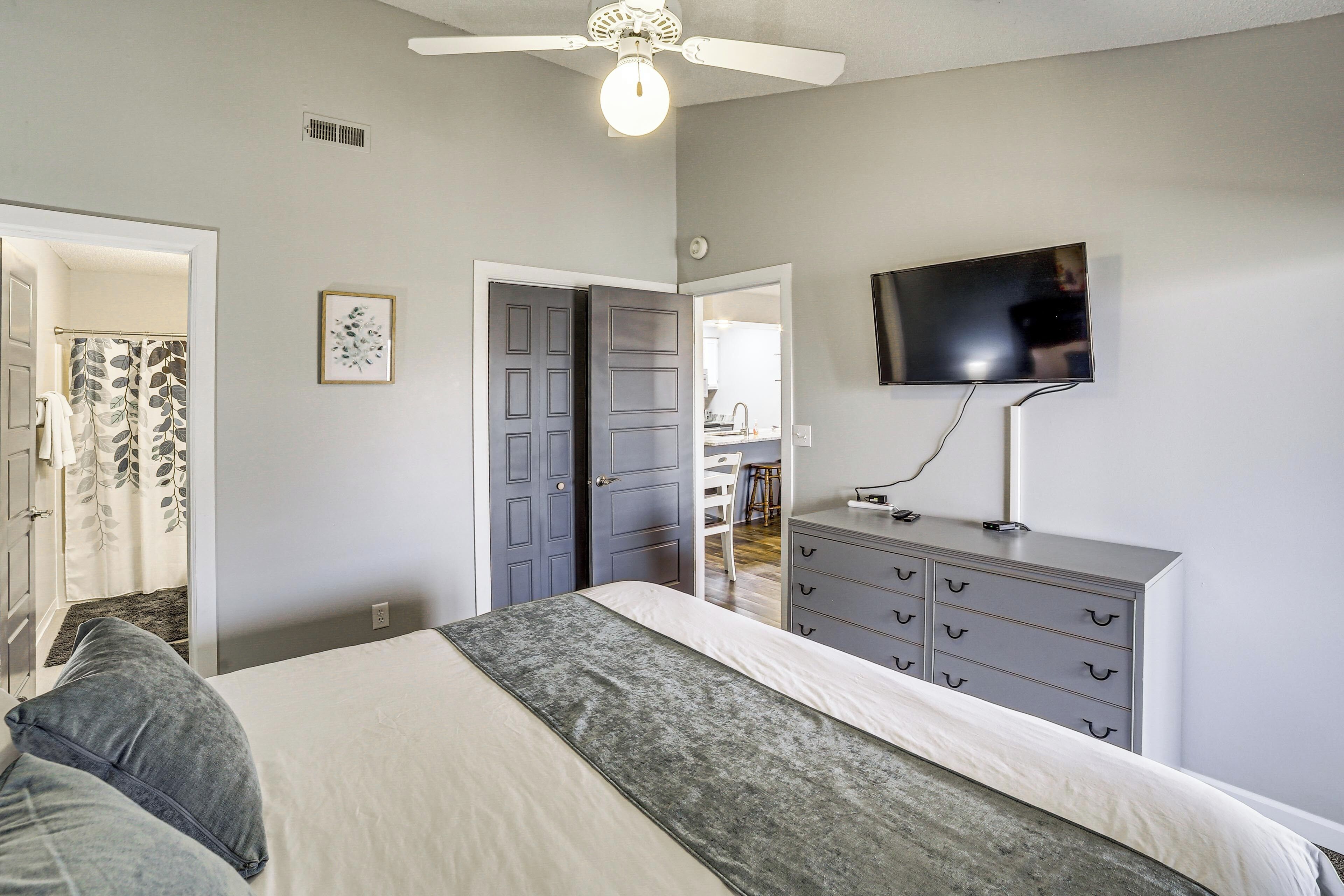A bedroom with a bed, a dresser, a television, and a ceiling fan.