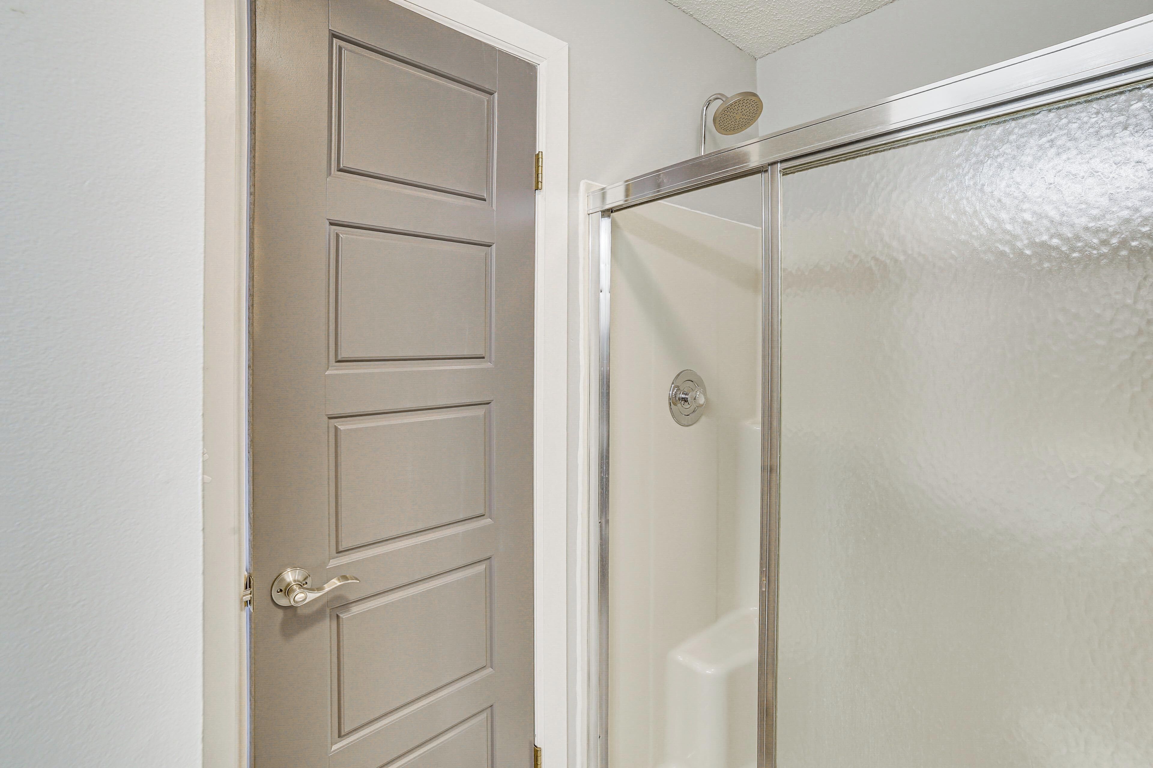 A bathroom with a white door, a glass shower enclosure, and a white textured wall.