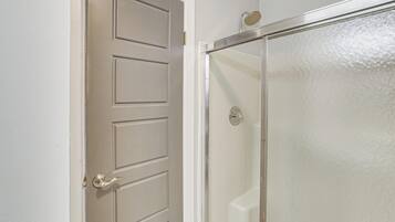 A bathroom with a white door, a glass shower enclosure, and a white textured wall.