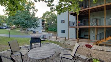 Un patio al aire libre con una mesa redonda y sillas, una parrilla y un pequeño jardín.