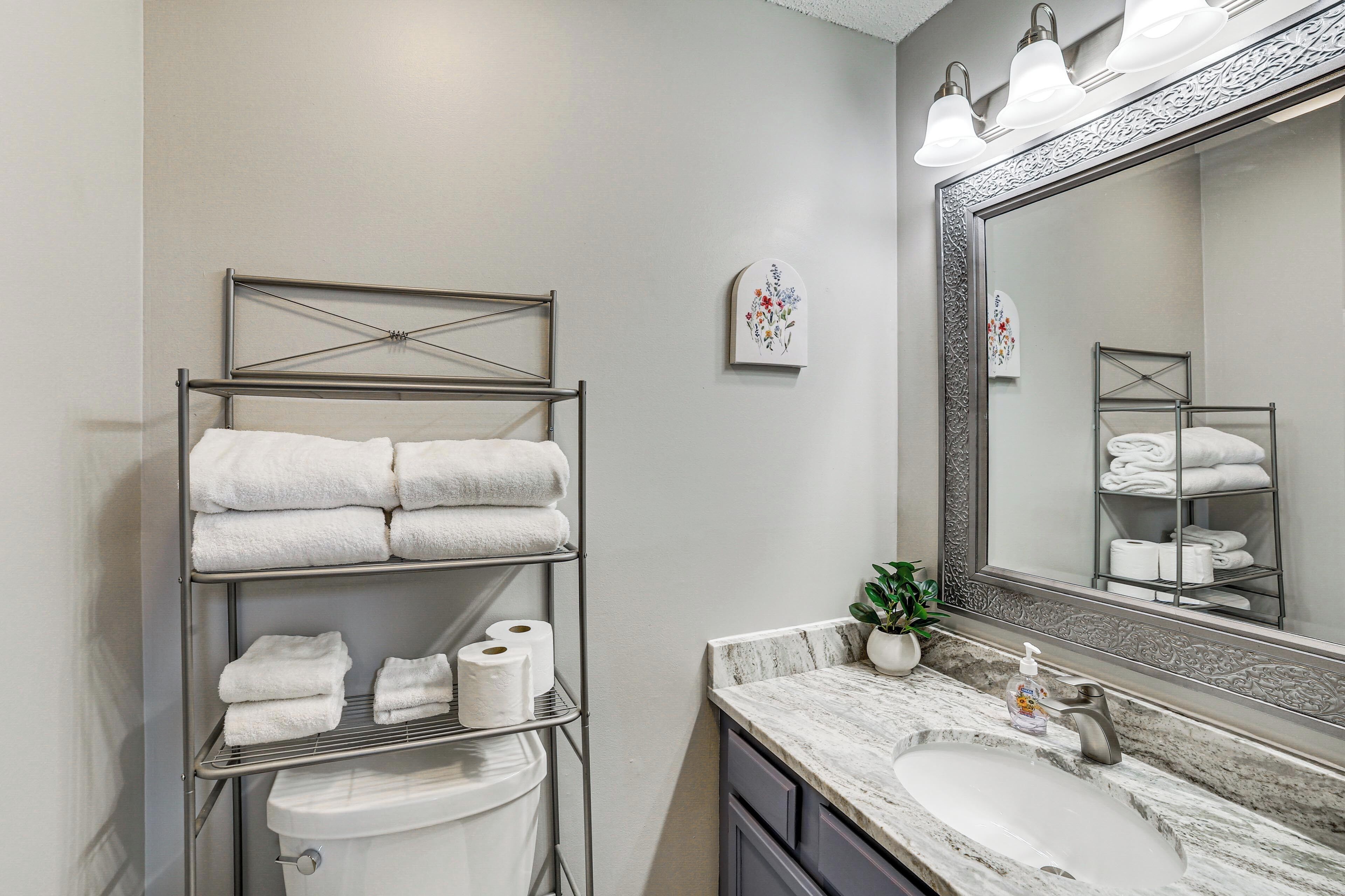 A bathroom with a metal towel rack, a sink, a mirror, and a potted plant.